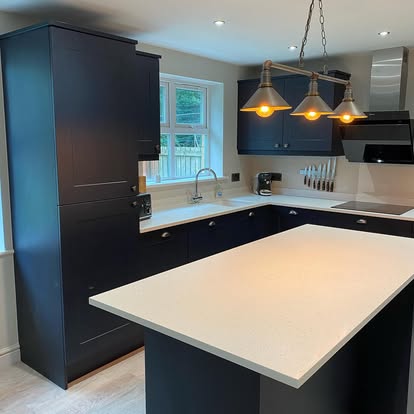 Spacious navy shaker kitchen with white countertops, large central island, brass pendant lights, stainless sink, and light wood flooring.